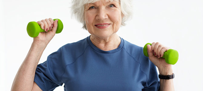 People, age, sports and active lifestyle concept. Picture of happy positive mature retired woman in t-shirt doing exercise with free weights in gym. Excited senior female training with dumbbells